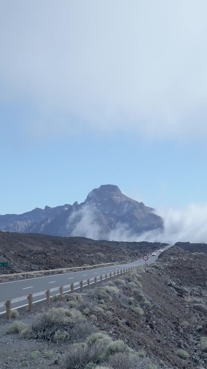 Auto che percorrono una strada di montagna attraverso un paesaggio vulcanico con nuvole.
