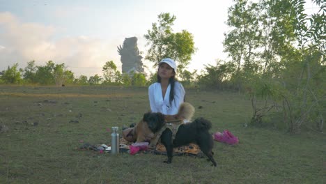 Beautiful-Indonesian-girl-with-white-dress-having-a-picnic-with-two-small-dogs-on-a-natural-lawn
