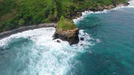 waves crashing on rocky cliff of menganti beach, kebumen in indonesia