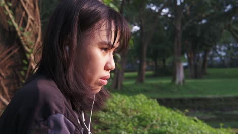 Close-up-view-of-young-female-adult-taking-off-earphones-and-looking-across-a-nature-park