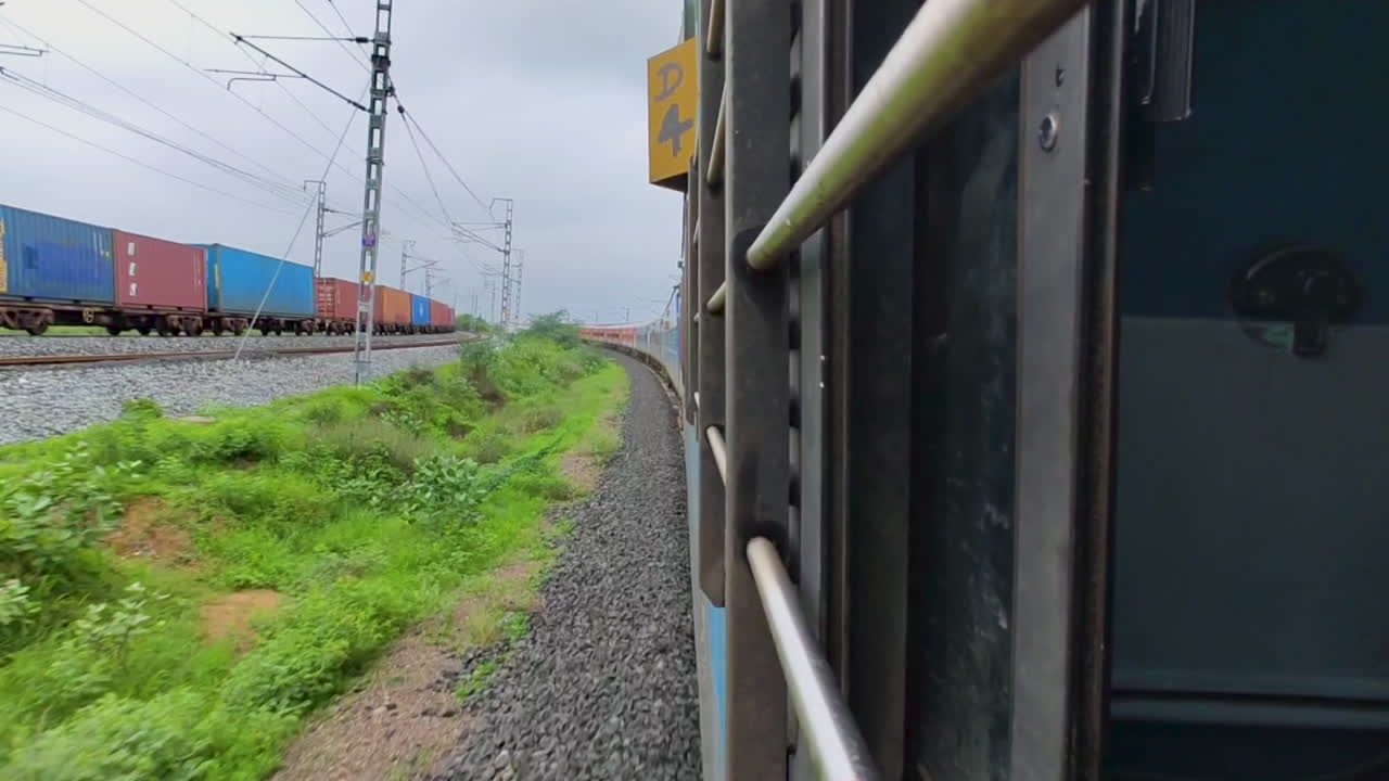 View from train window, freight trains as they pass on adjacent track in India.