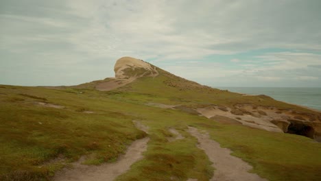 Low-handheld-shot-while-walking-down-a-path-to-the-plateau-on-top-of-a-sea-arch-in-New-Zealand