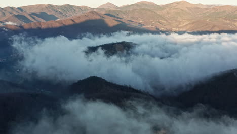 misty mountain peaks emerging through dense cloud cover, captured from an aerial perspective at dawn