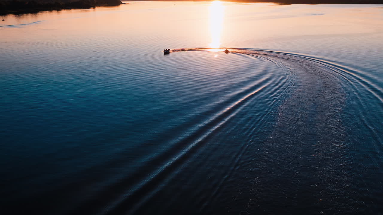 Motion of boats at sunset. Amazing view on the evening river with motor boat leaving paths on water surface. Aerial view.