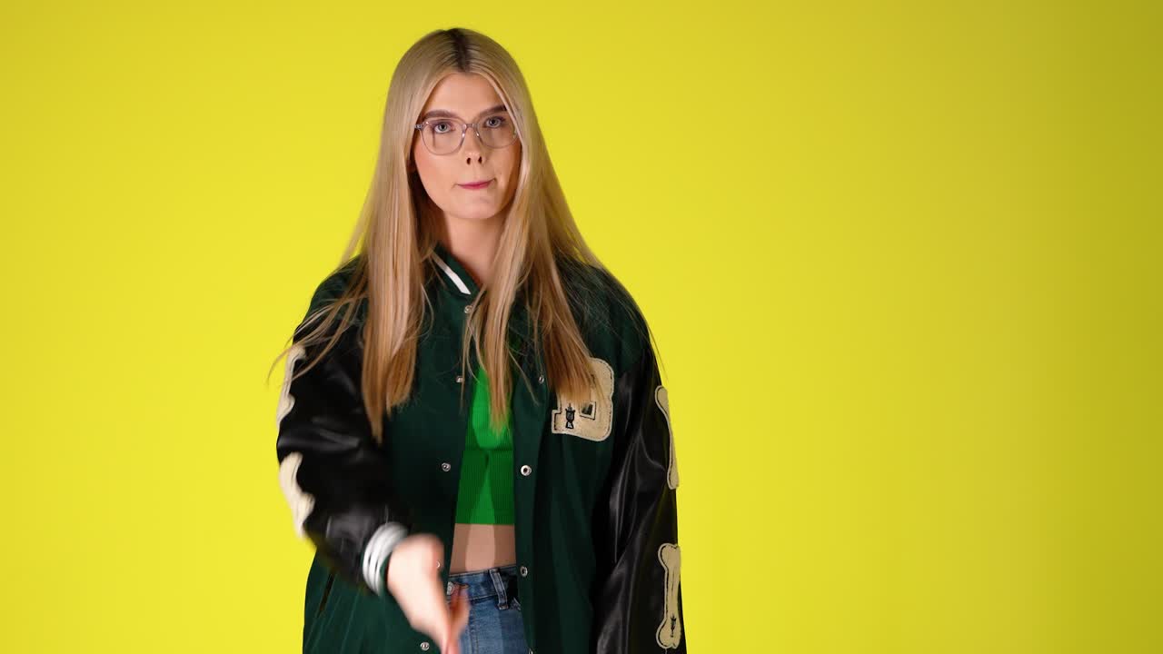 Giovane donna bionda che fa un gesto minaccioso con la mano a forma di pistola, scatto in studio colorato