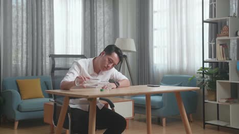 술에 취한, 우울한 아시아 남자가 테이블 위에 스마트폰을 들고 집에서 술을 마시기 전에 크 컵에 보드카를 부어 놓습니다.