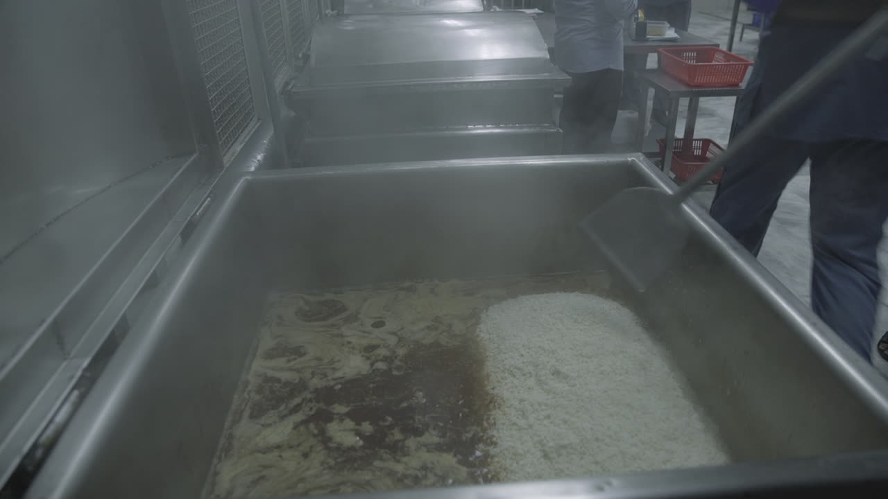 línea de producción de comida preparada en una fábrica, una vista de cerca de un hombre metiendo arroz en una máquina y agitándolo