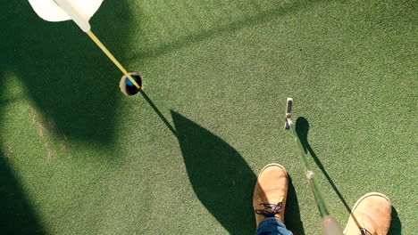 man sinks a blue golf ball into hole during minigolf game