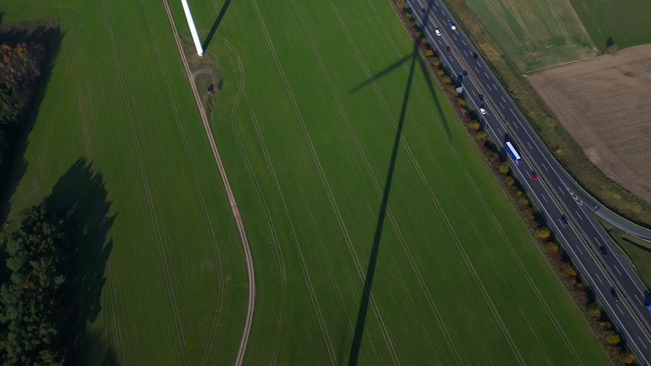 Wind farm turbines generating clean power in green fields next to a busy highway. Great aerial view flight tilt up drone