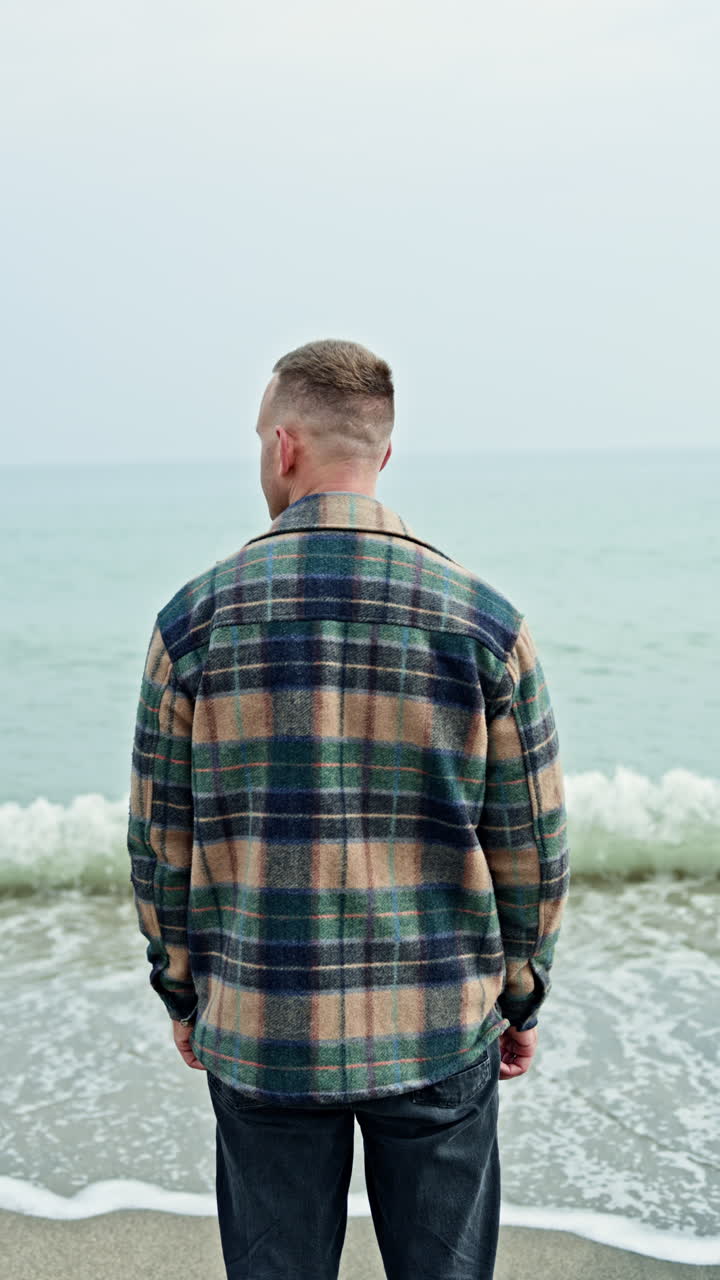 A man stands and looks at the sea. A man walks on the beach and looks at the waves. A young man dreamily walks along the shore near the ocean in autumn