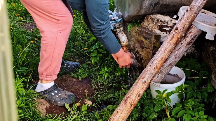 Woman washing hands under outdoor tap after work in backyarda