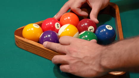 el hombre ajusta, desordena y juega con el estante de diamantes de la piscina de 9 bolas y aprieta las bolas con las manos antes de levantar el triángulo de madera en el primer plano del lugar en una mesa con fieltro verde o tela