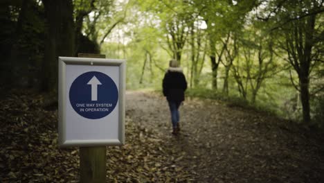 one way system in operation signage in the forest of kennall vale in cornwall, uk with woman walking on the trail