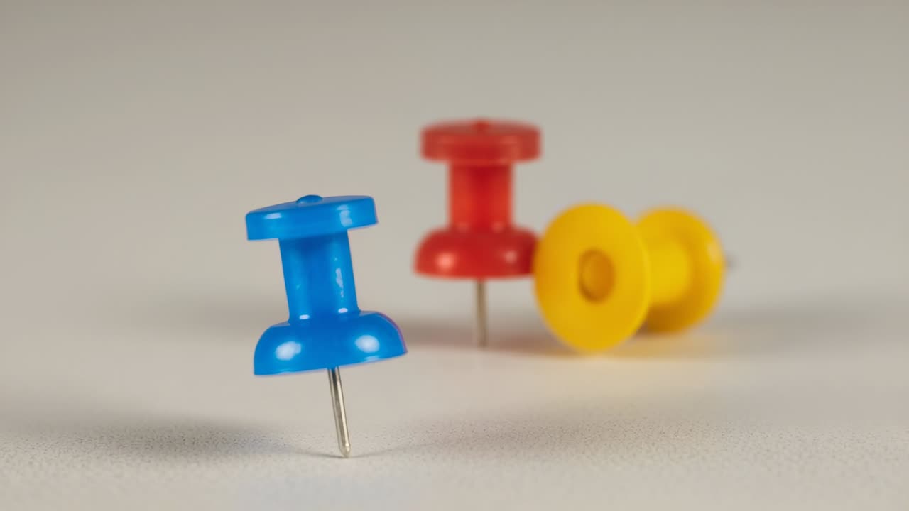Camera focus plane gradually shifting on tabletop revealing blue red yellow push pins in succession
