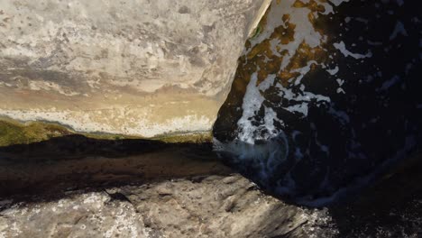 Water-flows-through-the-erosion-channel-in-a-rock-into-the-pools-below-in-the-Giant's-Cauldron-near-Alicante,-Spain---ascending-aerial-view