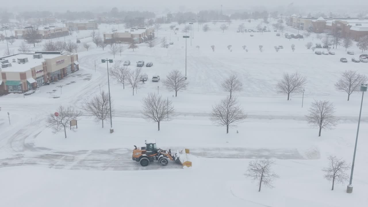 Automated snowplow machine removing snow from roads near shopping centre during blizzard.