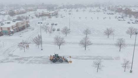 automated snowplow machine removing snow from roads near shopping centre during blizzard.