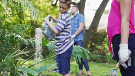 Smiling caucasian brother and sister gardening with parents, smiling and watering plants