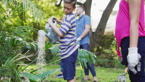 smiling caucasian brother and sister gardening with parents, smiling and watering plants