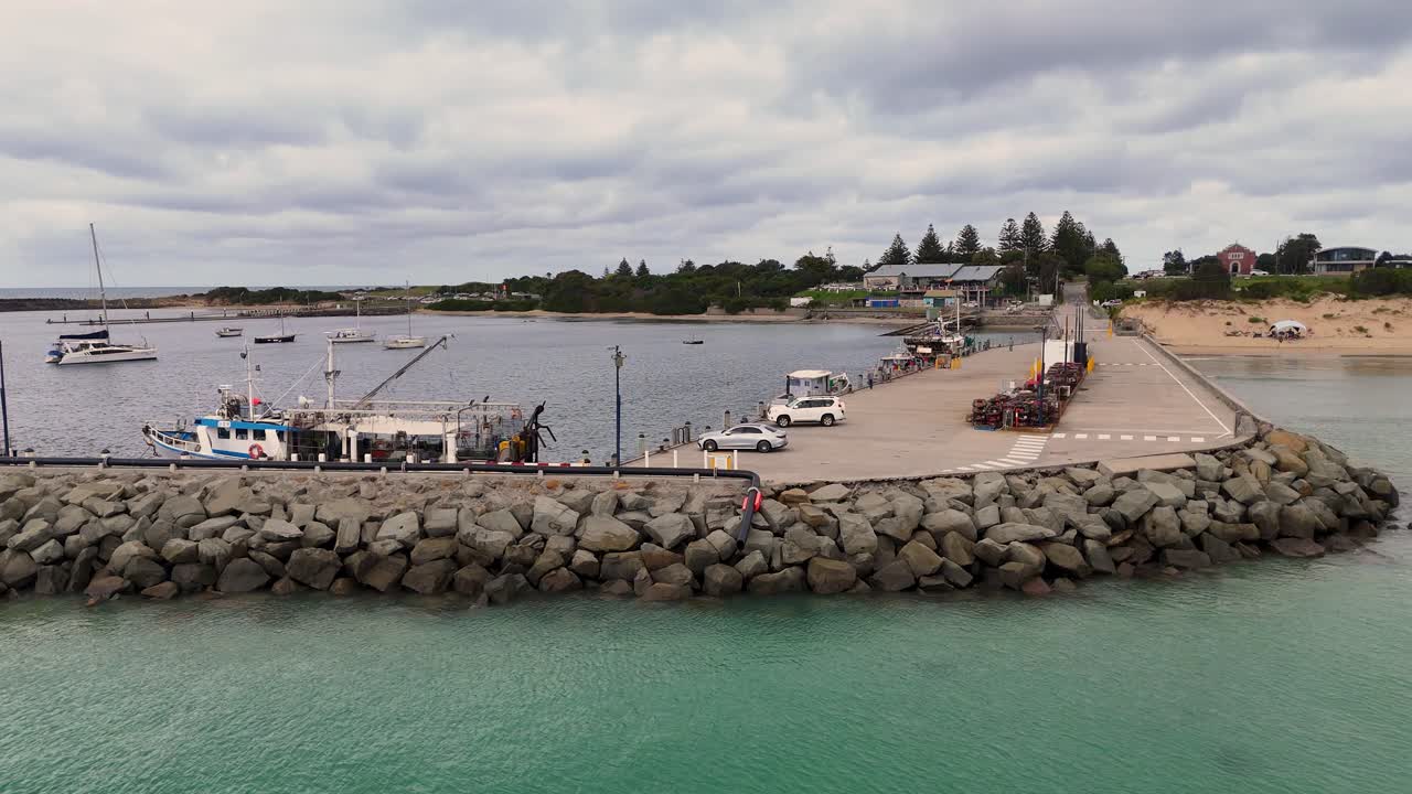 Drone footage captures Apollo Bay's harbor, showcasing boats, jetty, and rock wall under overcast skies
