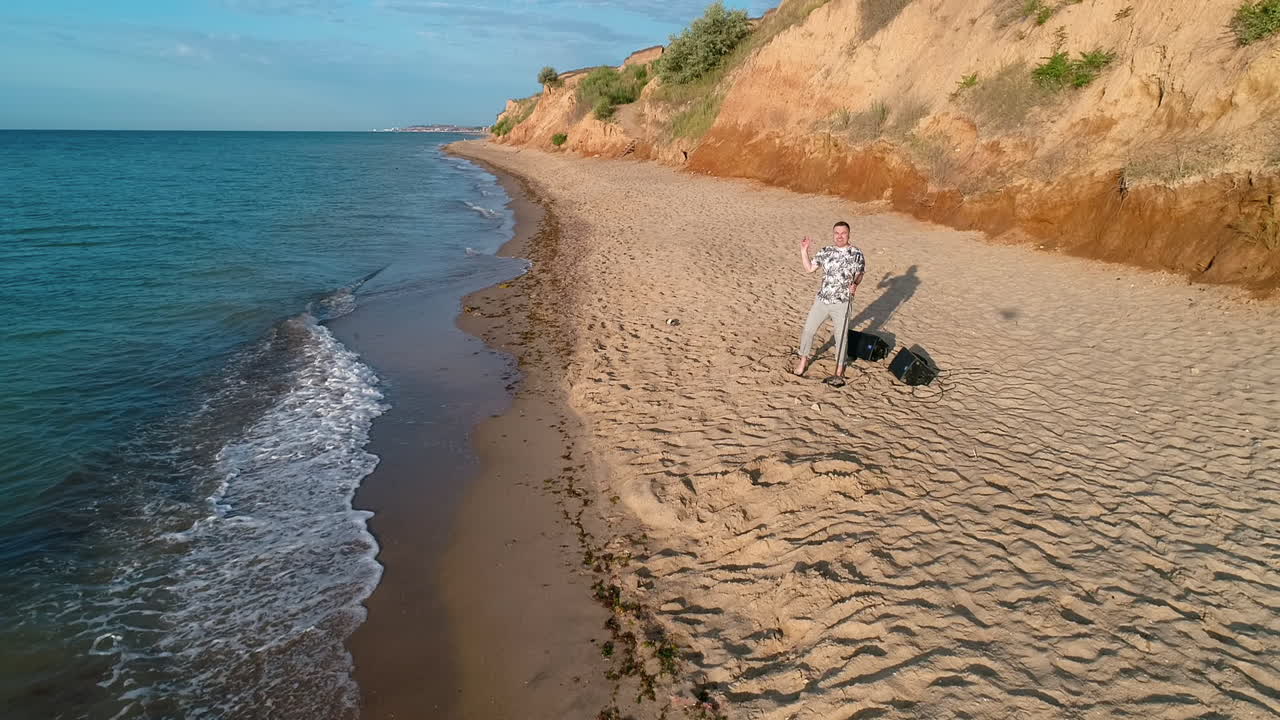 Young man singing to microphone. Aerial view of young man singing on the beach by the sea