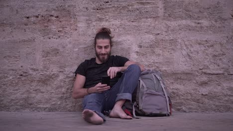 man sitting on the street with smartphone and backpack