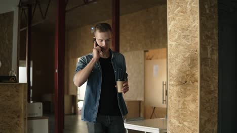 Gutaussehender-Junger-Geschäftsmann-In-Lässiger-Kleidung-Kommt-In-Einem-Modernen-Büro-Oder-Am-Arbeitsplatz-Zur-Arbeit,-Während-Er-Mit-Seinem-Handy-Spricht