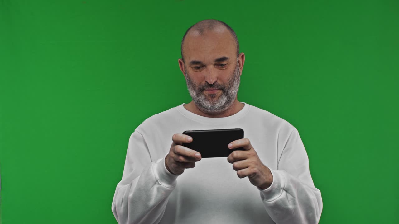 hombre emocionado con capucha jugando al juego en el teléfono móvil contra el fondo de la llave de croma verde