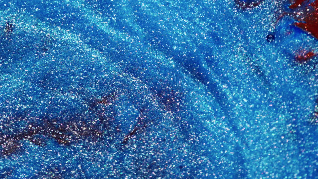 Close-up of shimmering blue and red glitter inks in motion, forming fluid wave-like patterns in a macro abstract composition
