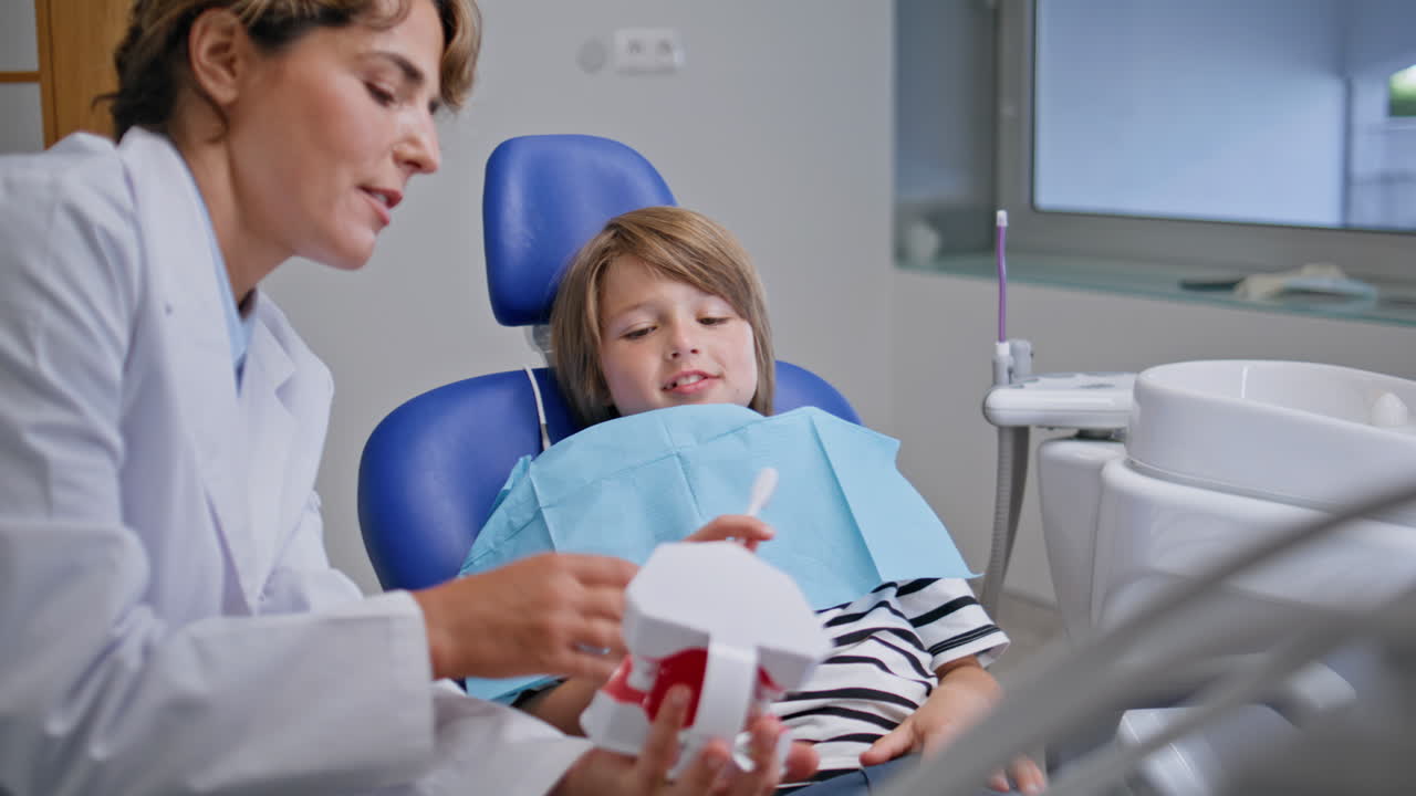 Dentist educating teeth hygiene to little boy in stomatology chair closeup