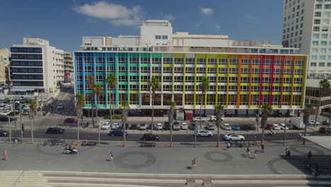 Disparo-De-Drones-Deslizantes-Frente-Al-Colorido-Hotel-Dan-En-Tel-Aviv,-El-Edificio-Rainbow-En-El-Paseo-Gordon-Y-La-Playa-Frishman-Llena-De-Visitantes-En-Un-Cálido-Y-Tranquilo-Día-De-Verano.