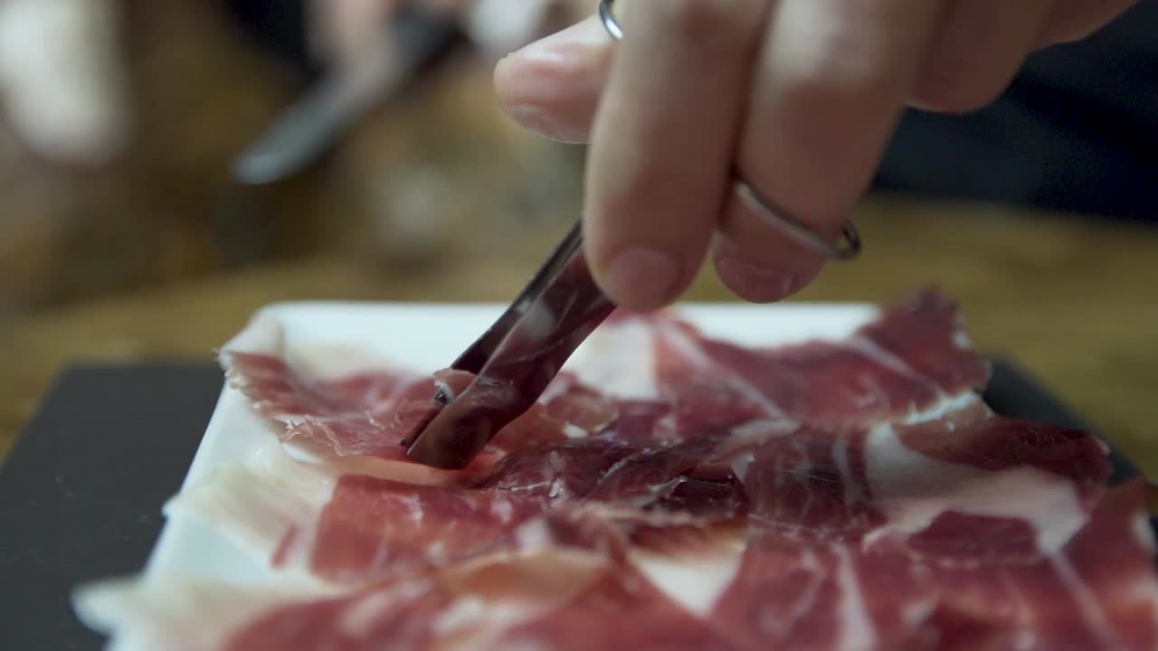 CloseUp of carefully sliced Serrano ham, gently laid on plate to serve