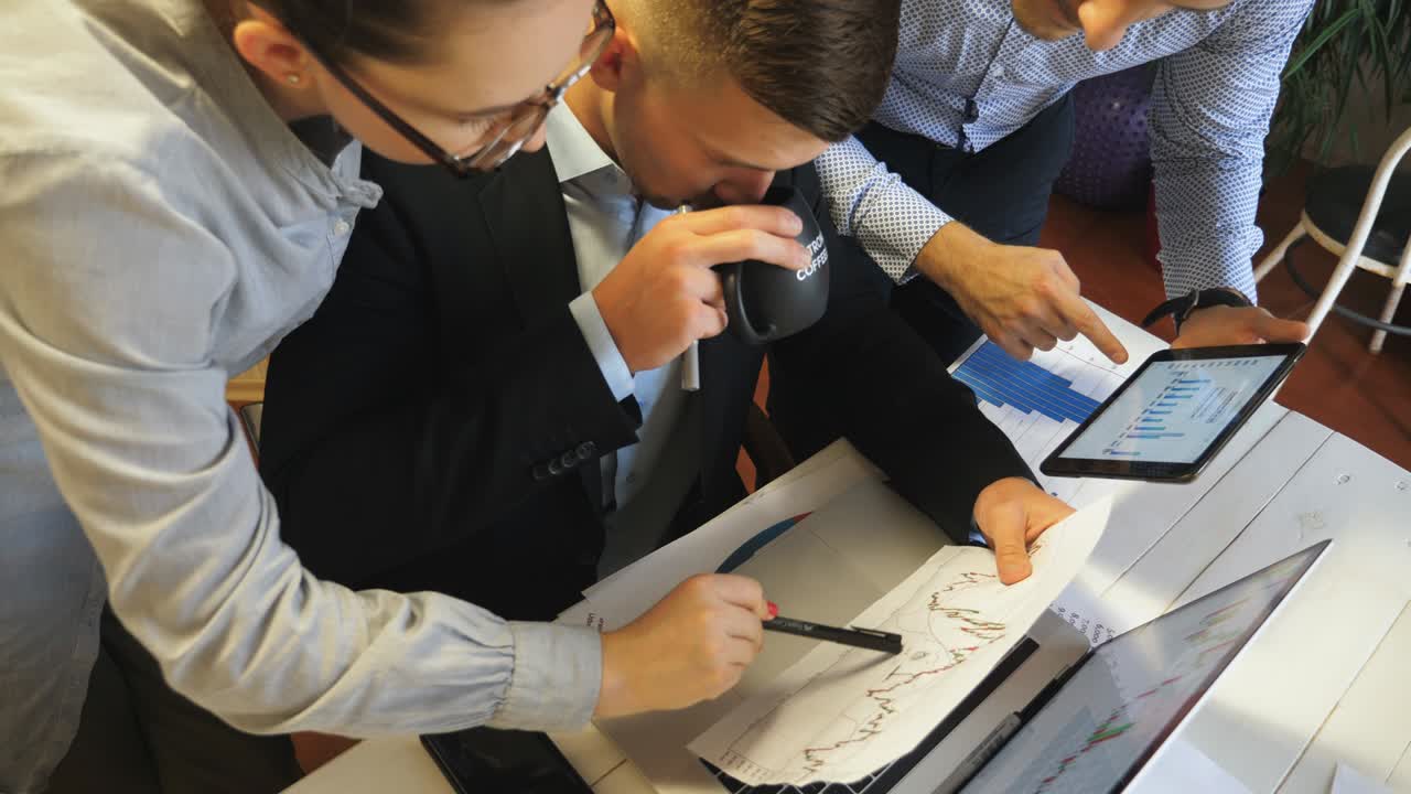 cerca de un grupo de empleados comparando el gráfico de resultados de ventas en papel con el gráfico en la pantalla de la tableta pc en la oficina. jóvenes colegas examinando informes financieros durante una reunión de negocios en el interior. movimiento lento