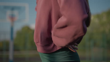 close-up of lady in green leggings with partial view of another lady in blue sweater, blurred background of an outdoor sports area, engaged in fitness exercise