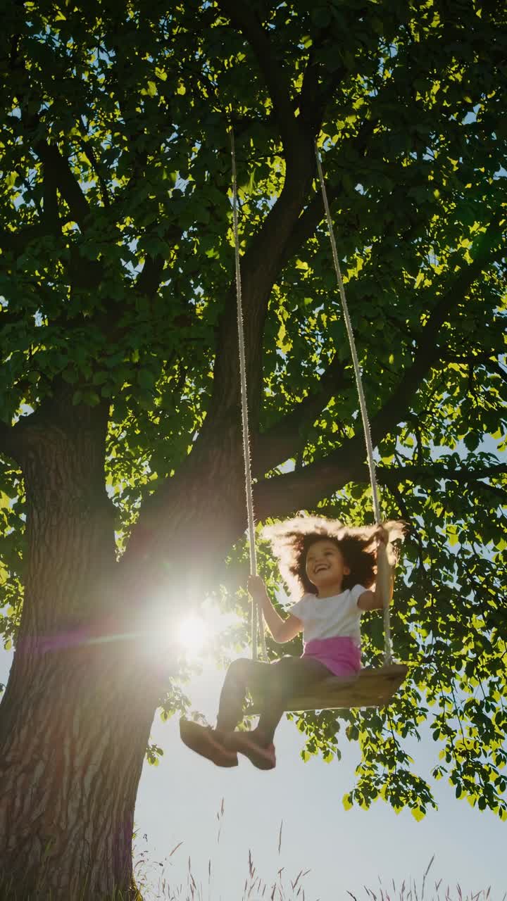 Video da angolazione bassa di un bambino felice che si dondola sotto un grande albero, catturando un momento giocoso e spensierato