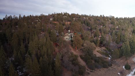 Low-push-in-aerial-shot-of-a-beautiful-mountain-cabin-overlooking-the-alpine-forest-during-the-winter-in-Big-Bear-Lake,-California