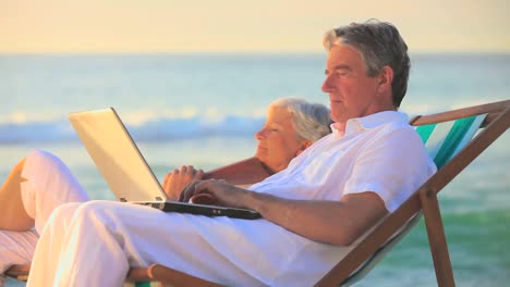 elderly man using his laptop while his wife is sleeping