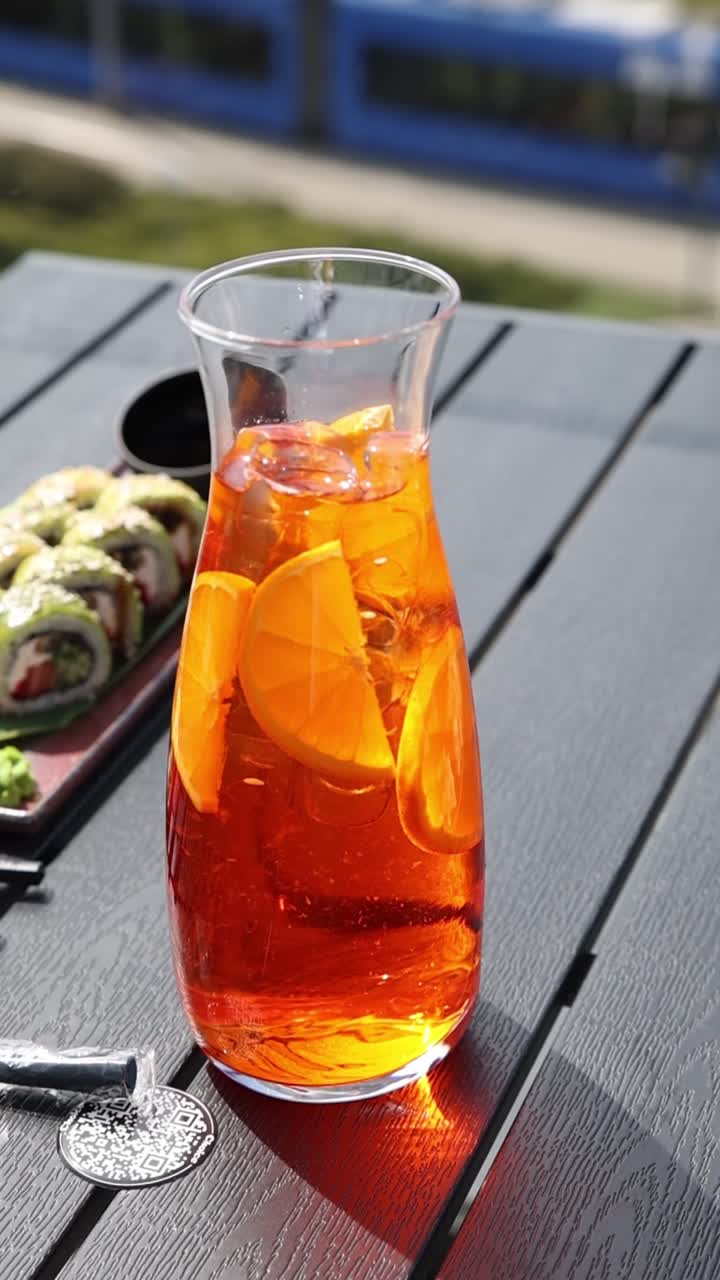 Brocca di bevanda rinfrescante all'arancia con ghiaccio e sushi su un tavolo all'aperto