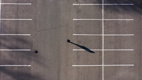 una toma de arriba hacia abajo directamente sobre un estacionamiento vacío con un hombre jugando con un auto eléctrico con control remoto