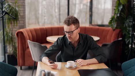 handsome young man sitting in a cafe receives a joyful message on a smartphone