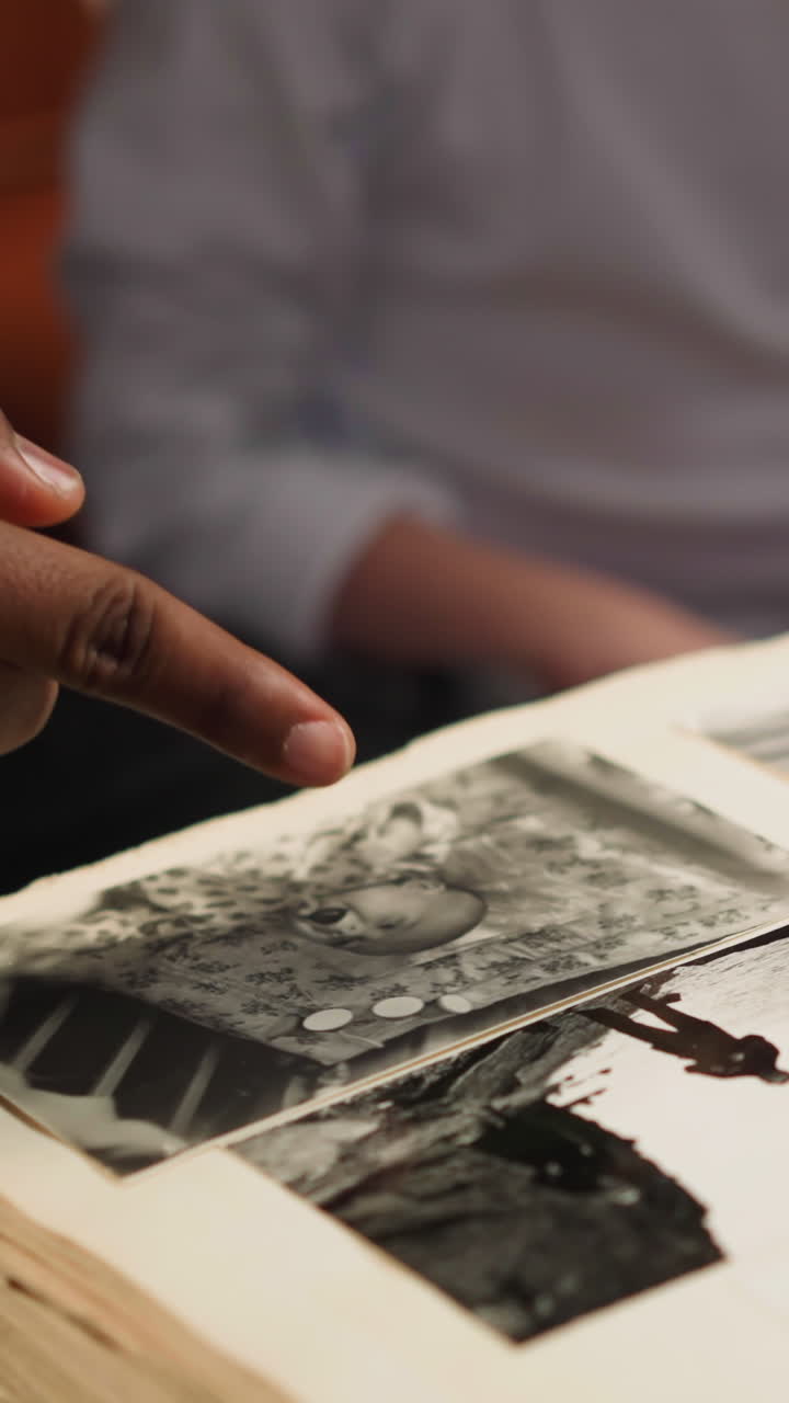African-American man points to faded photo and tells story about grandfather to little girl and woman groupmate at home closeup slow motion