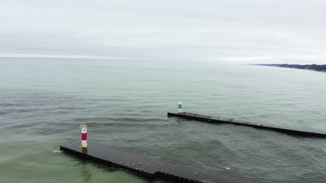 Aerial,-dirty-water-flows-out-to-sea-at-coastal-river-mouth-with-groyne-breakwalls