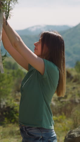 long haired woman ties ribbon and makes wishes on fir tree branch at highland side view. mystical traditions. tourist spends time at eco resort