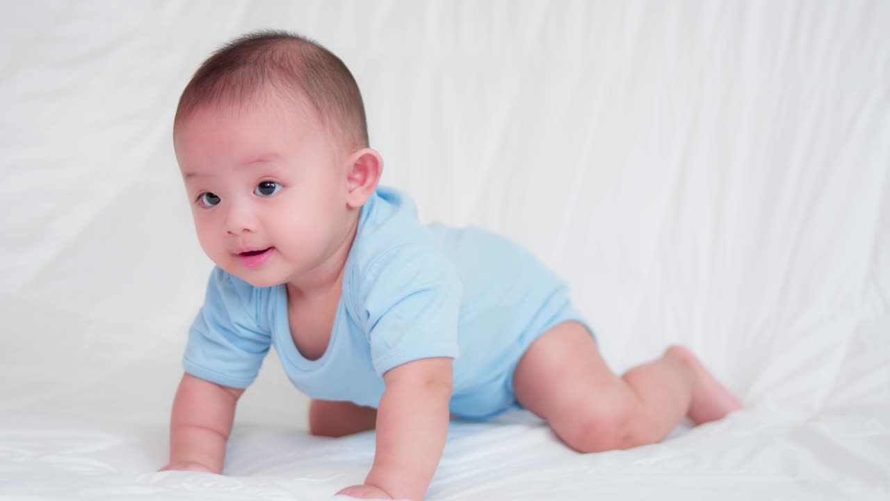 Happy family, Cute Asian newborn baby wear blue shirt lying, crawling play on bed looking at camera with laugh smile happy face. Innocent little new infant adorable. Parenthood and Mother Day concept.