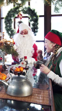 hungry elves eating with santa at festive table. elves drinking tea with santa in a room with christmas decorations. vertical video