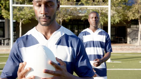holding rugby ball, african american man focusing while teammate stands behind on sports field