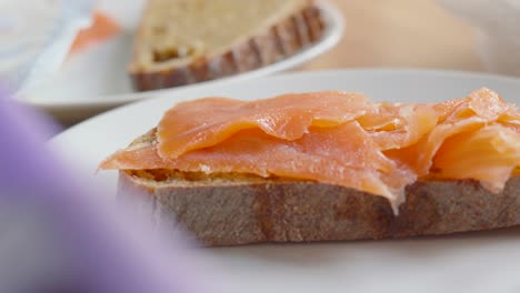 slices of scottish smoked salmon carefully placed on sourdough bread by female hands for healthy morning breakfast