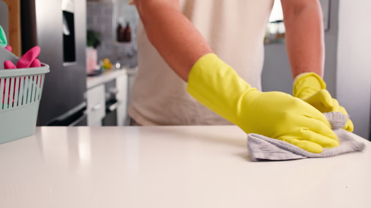 Manos con guantes amarillos limpiando la encimera de la cocina manchada