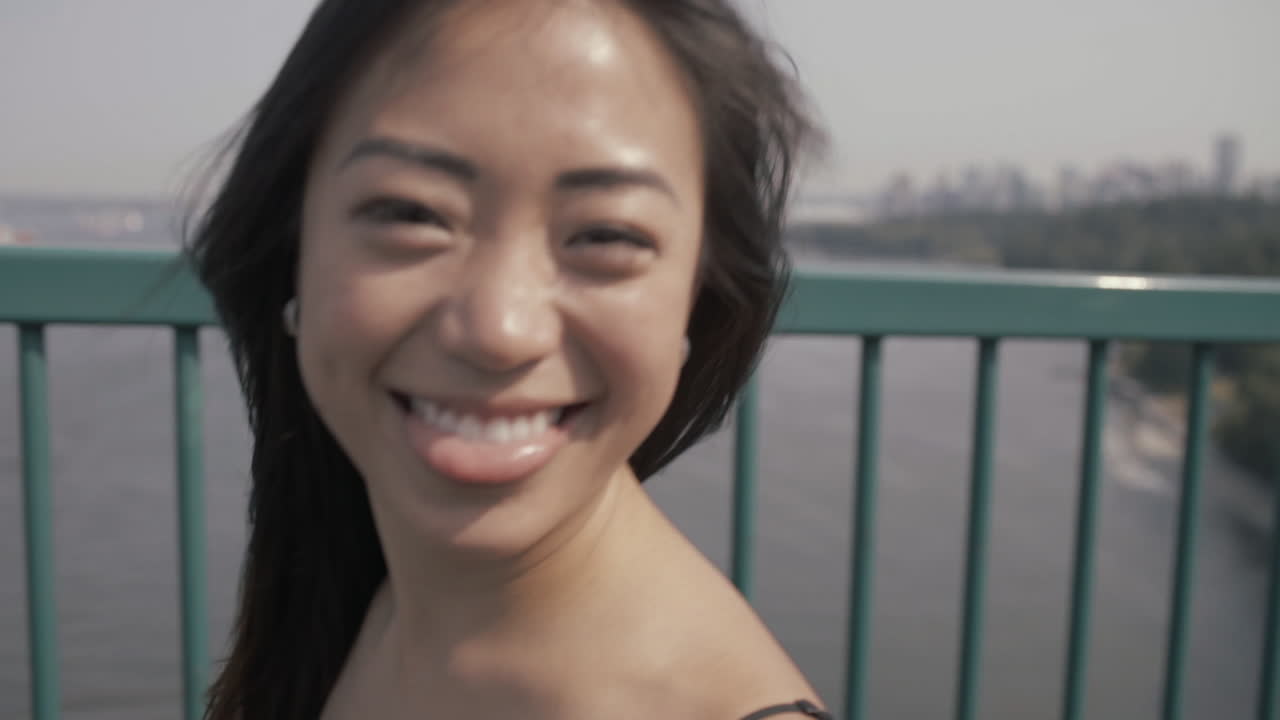 밴쿠버의 라이온스 게이트 브리지에서 우스꽝스러운 웃는 얼굴을 하고 있는 귀여운 아시아 소녀의 클로즈업 샷, slowmo