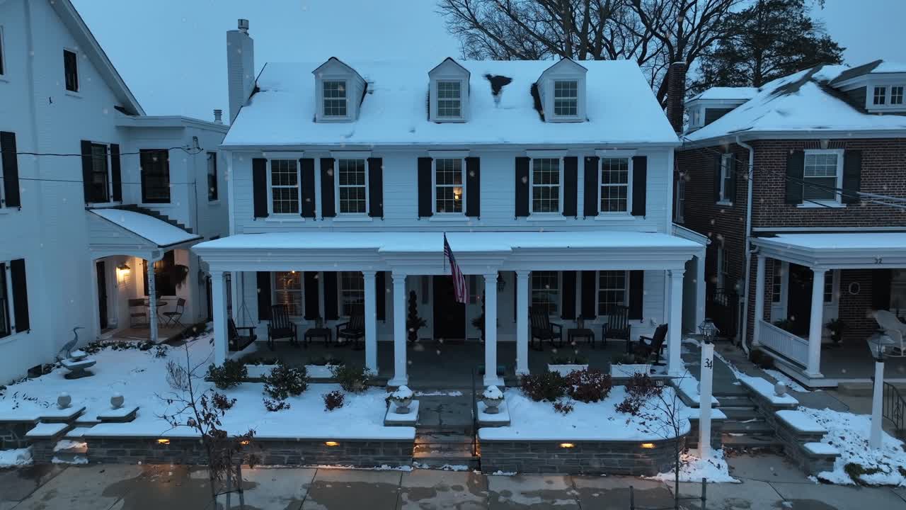 Snowy Two Story Building with american flag at Front Exterior of House. Snowflakes falling from sky. Family time in Christmas Season. Aerial approaching shot.